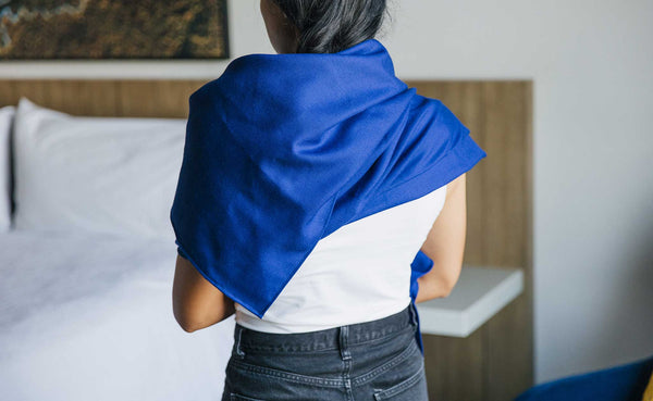 A Large Shepherd's Wool Utility Cloth in Neela Blue being worn as a scarf, artfully arranged at the back of the neck/shoulders.